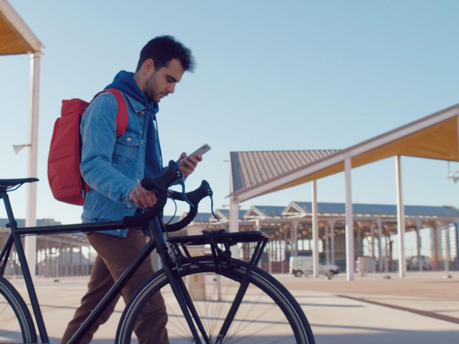 A man walking with a bike, looking at his mobile phone